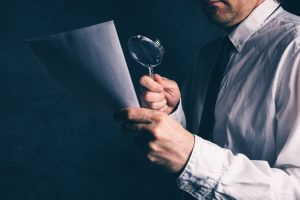 Tax inspector doing financial auditing, businessman reading business report or contract footnotes disclaimer with magnifying glass, retro toned, selective focus